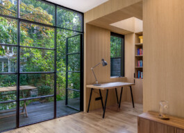 Serene work space with a view of the garden through a large metal-framed glass facade in IJarchitecture's Amsterdam extension project.