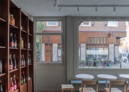 Interior view of Saint-Jean Deli featuring a display cupboard on the left and large windows overlooking the street and buildings that mirror the shop's material palette. Interior design by Ivo Jelinek of IJarchitecture. Photo by Irena Mila.