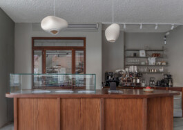 Central island counter with glass display at Saint-Jean Deli, kitchen door on the left, and coffee preparation pantry on the right, designed by IJarchitecture. Photo by Irena Mila.