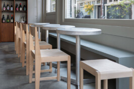 Aluminium Frama cafe tables lined with Frama light wood chairs and a long bench against the window at Saint-Jean Deli by IJarchitecture. Photo by Irena Mila