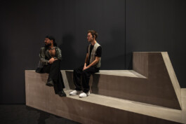Two visitors seated on the geometric bench at the Life in Different Resolution exhibition, absorbed in the art of Random International.