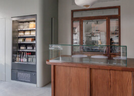 The wooden counter with a glass vitrine at Saint-Jean Deli, featuring a door to the kitchen and a to-go fridge filled with beverages on the left. Interior designed by architect Ivo Jelinek of IJarchitecture. Photo by Irena Mila.