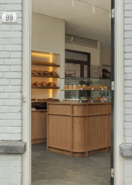 Entrance view of Saint-Jean Deli in Amsterdam, designed by IJarchitecture, showing the oak counter, glass vitrine and bread display.