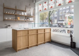 Main interior of Saint-Jean Bakery in Amsterdam by IJarchitecture, featuring an oak counter with a custo made concrete slab, FRAMA shelving, terrazzo floor and large front window. 